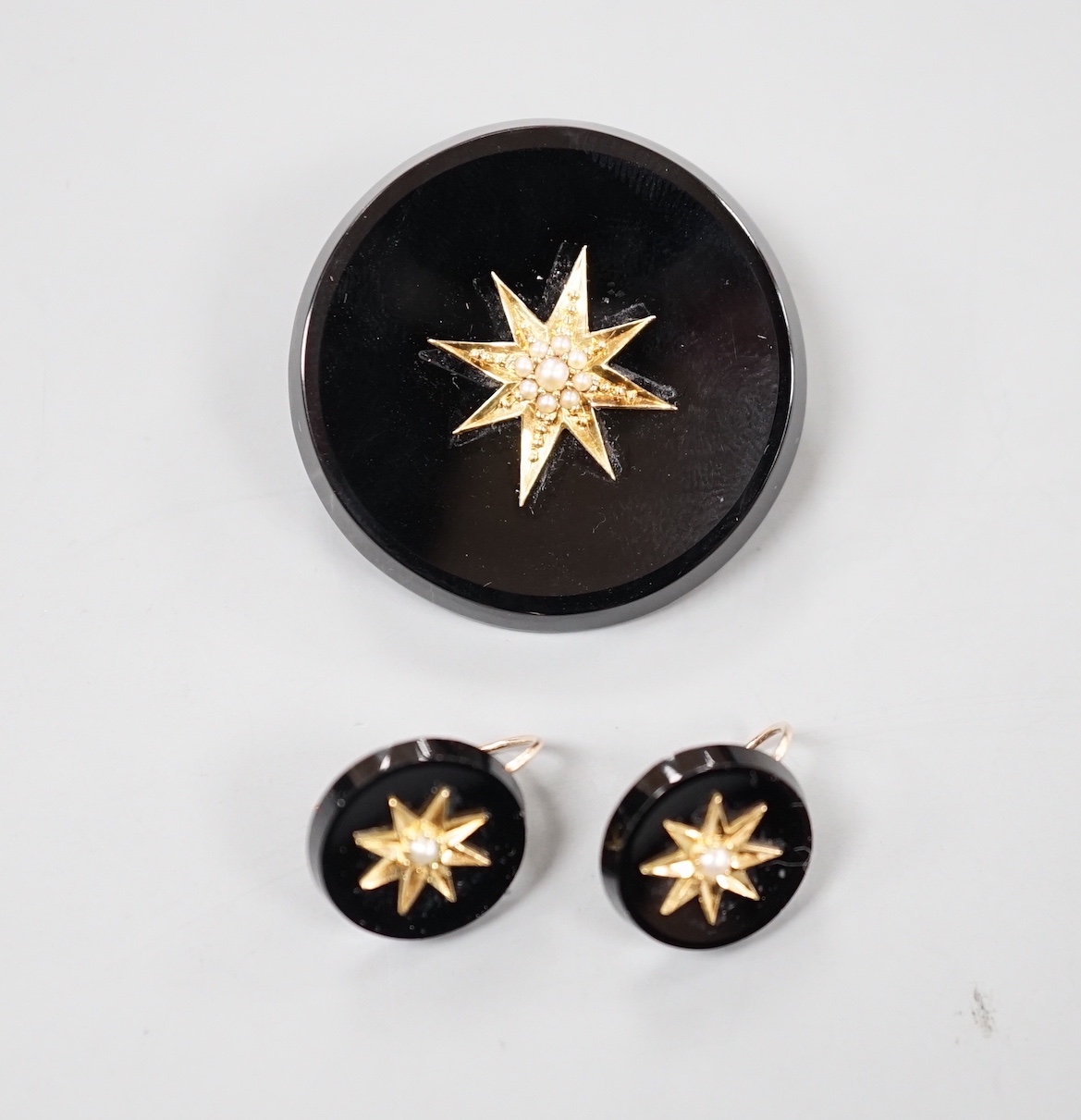 A late Victorian suite of yellow metal mounted black onyx and seed pearl mourning jewellery, coimprising a brooch, 33mm and pair of earrings.